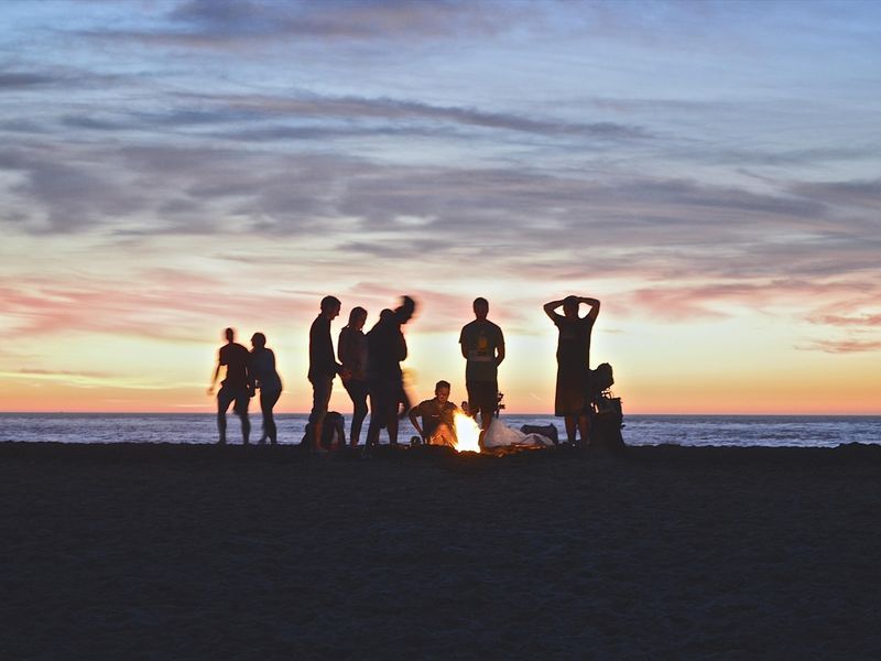 Friends hanging out on the beach near the campfire - Benefits of celebrating a birthday outdoors - Image