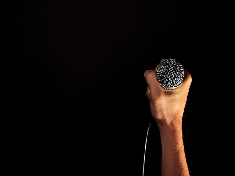 Male hand with a wired microphone in his hand on a black background - Karaoke birthday party ideas - Image