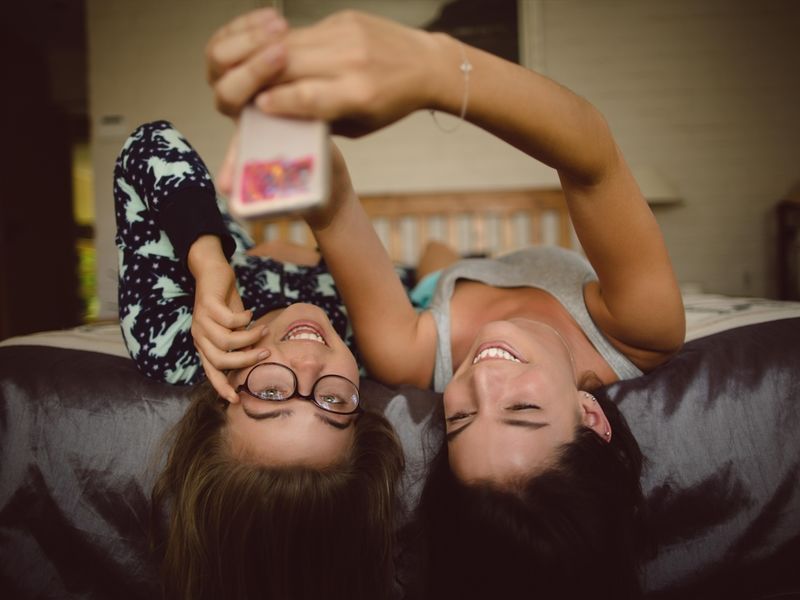 Two girls lie on the bed and look at the phone screen - How to throw a slumber party for adults on their birthday - Image