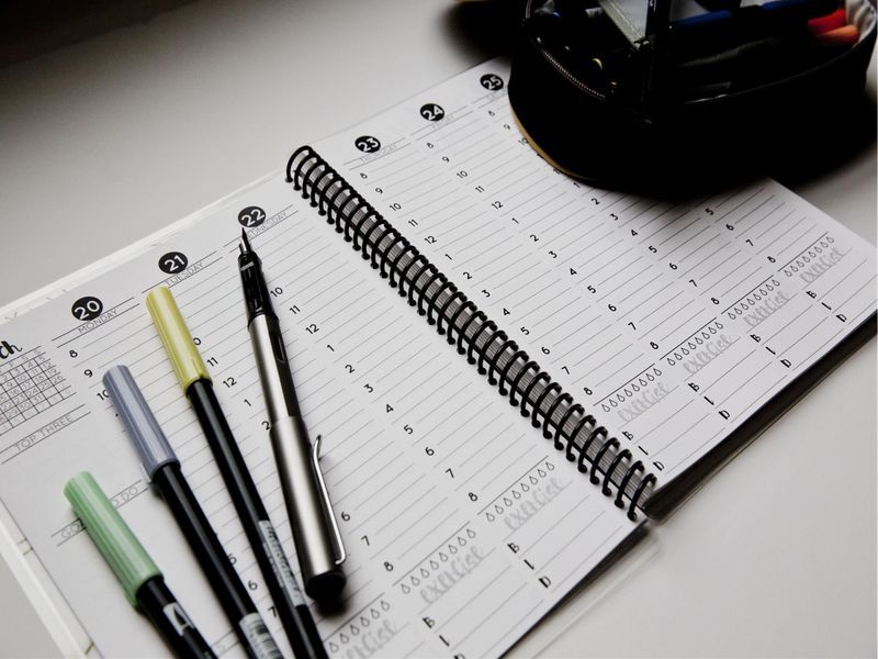 A planner notebook and pens lie on a white table - Stay organized - Image