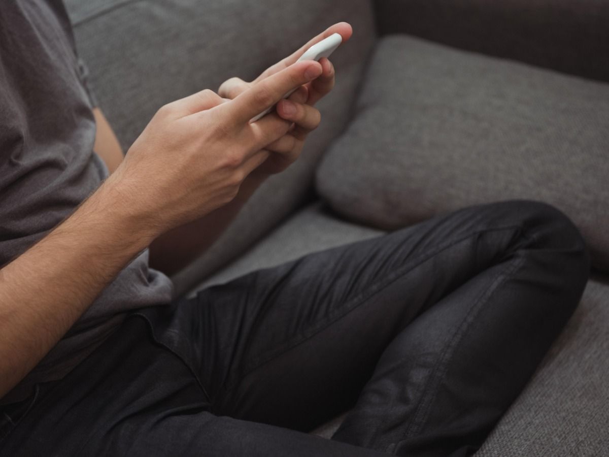 A man is sitting on the sofa with a phone in his hands - Keep mobile device users in mind when choosing images for your blog - Image