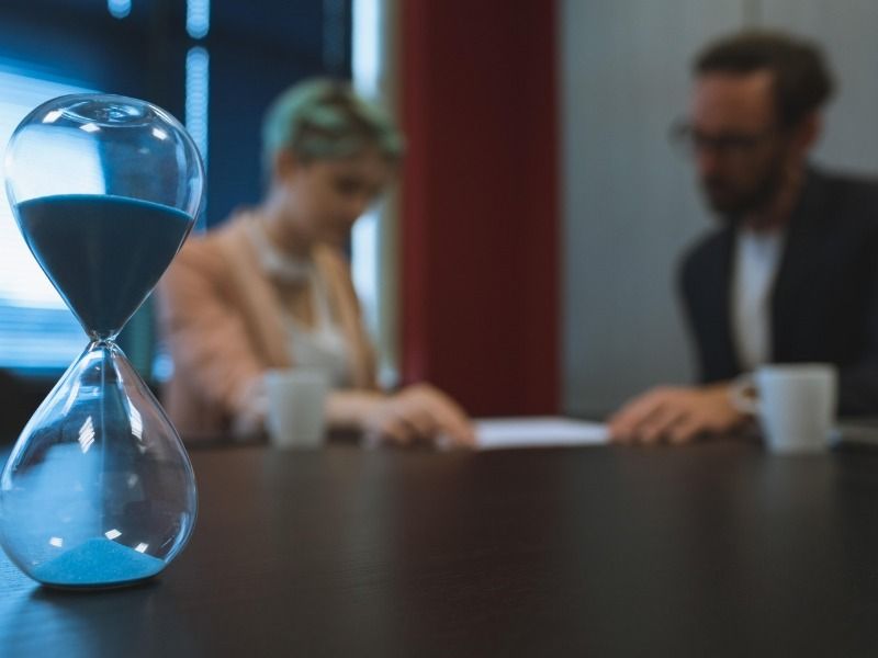 Close-up of a glass hourglass with coworkers in the background having a discussion - Use third-party tools for effective Instagram marketing - Image