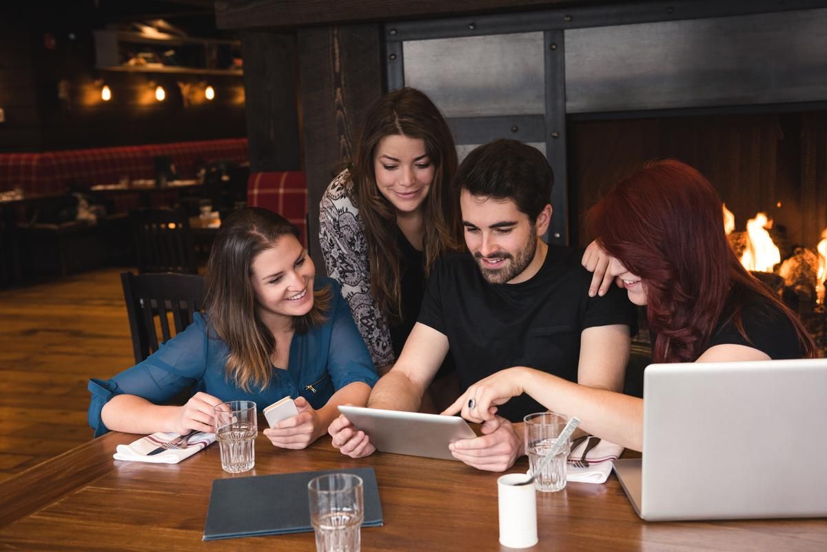 Un grupo de cuatro personas en un restaurante está viendo algo en una tableta - Una guía completa sobre cómo conseguir más vistas en YouTube - Imagen