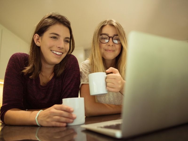 Two young women with cups of coffee look at a laptop screen - How to make a YouTube video in 5 simple steps - Image