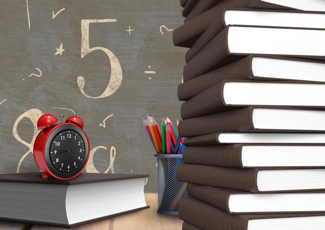 Alarm clock on a book with number and mathematical symbols on chalkboard in background - Image
