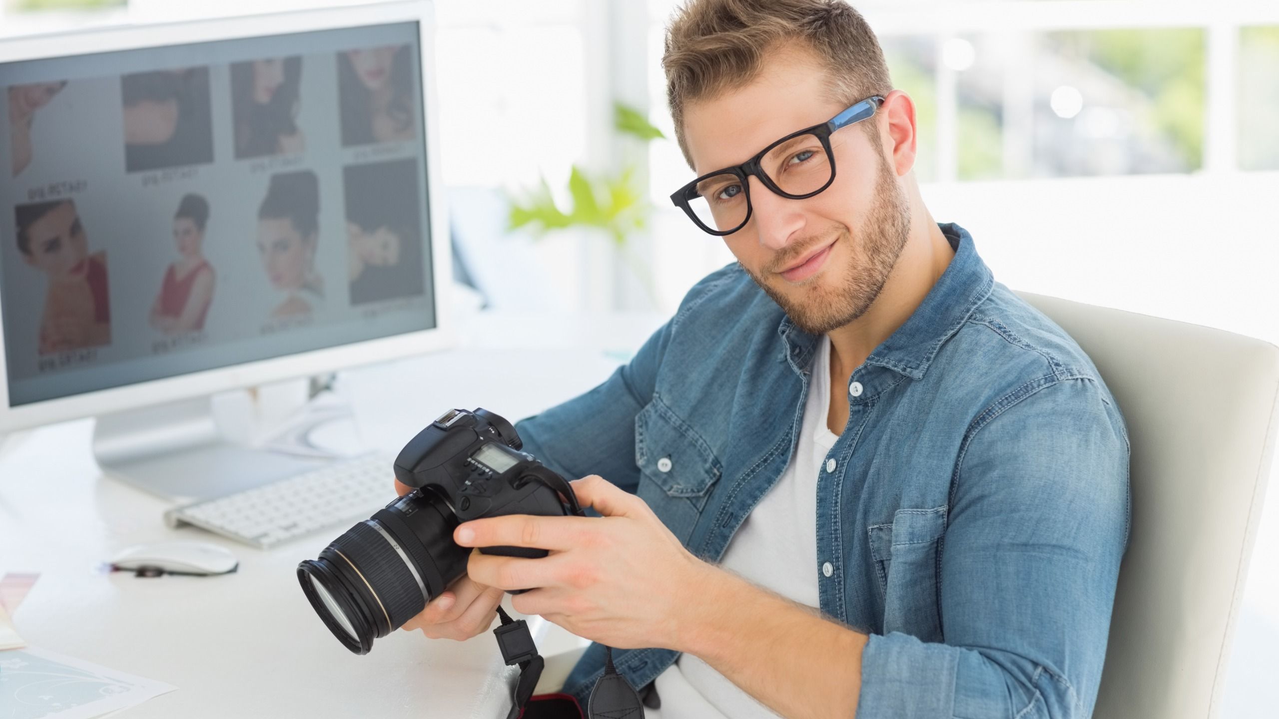 A male photographer sits at an office desk with a digital camera and smiles at the camera; TikTok profile picture - Tips for choosing the best profile photo for different social networks - Image