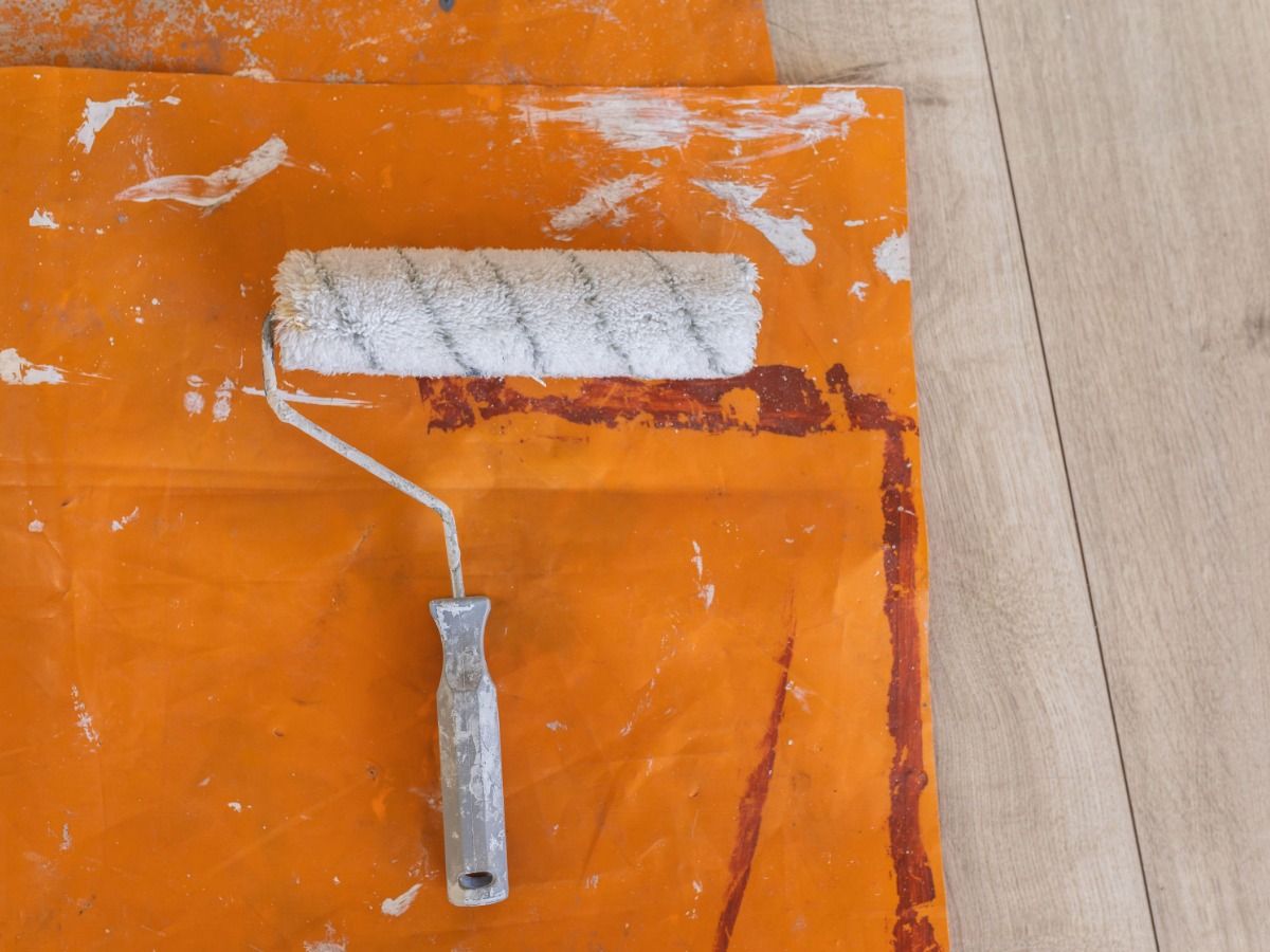 Rodillo de pintura sobre cubierta de plástico naranja sobre suelos de madera