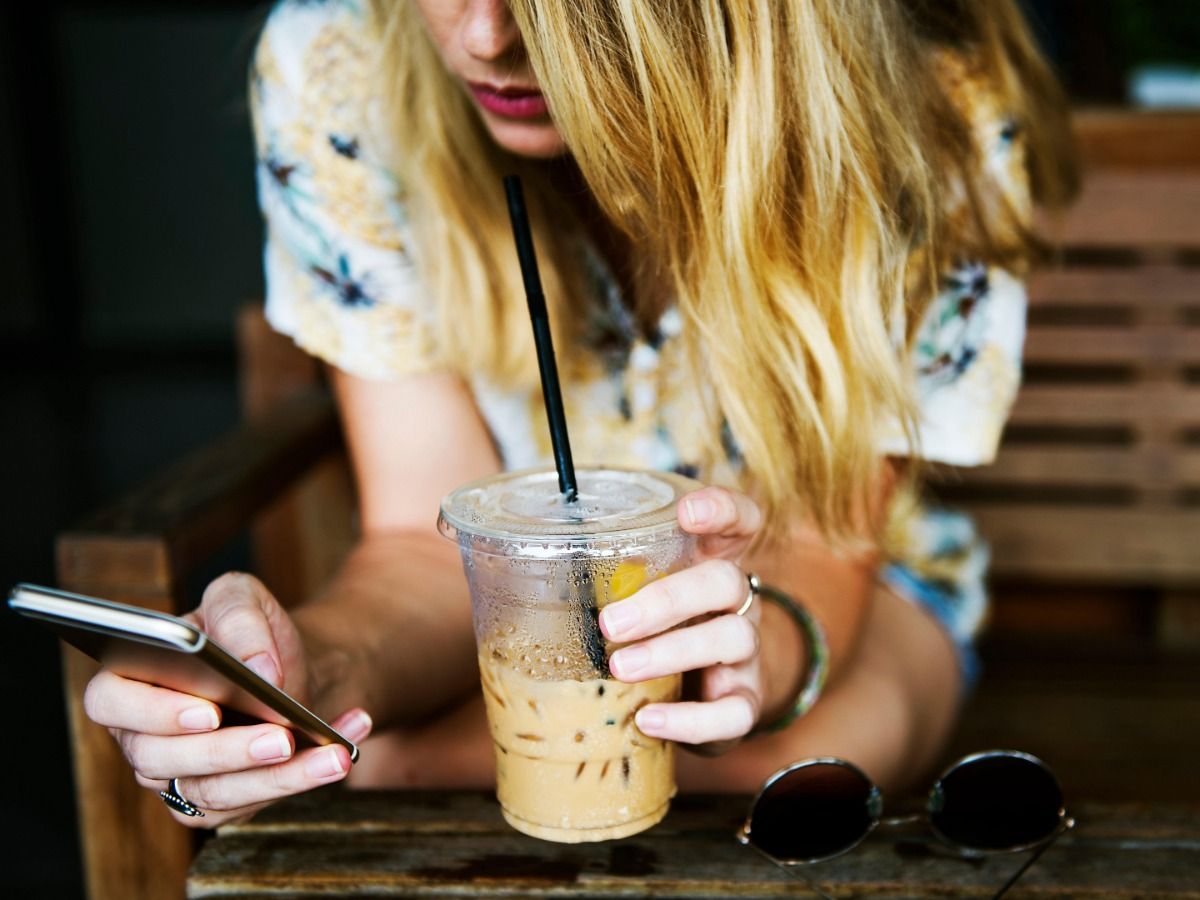 Blonde Frau trinkt Eiskaffee und benutzt Smartphone