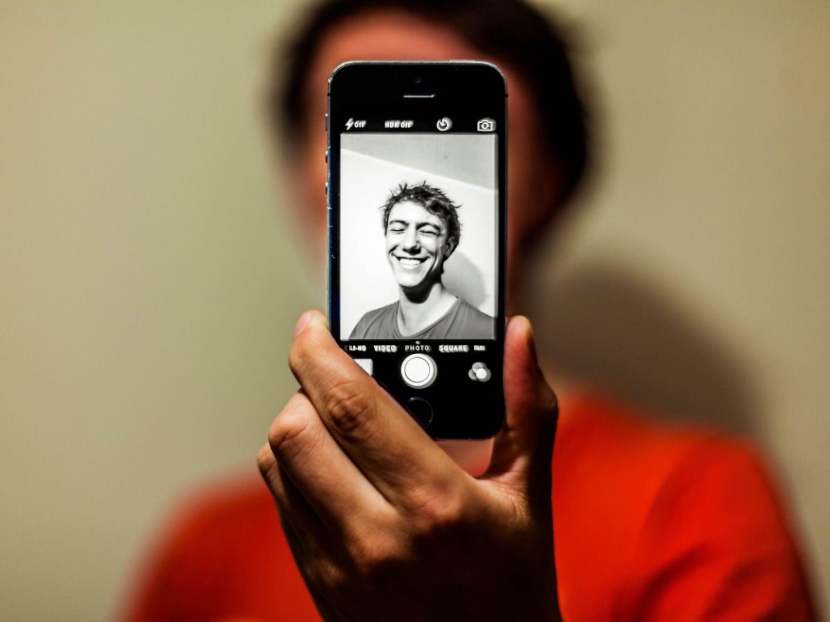 Persona con teléfono inteligente frente a la cara para tomar selfie