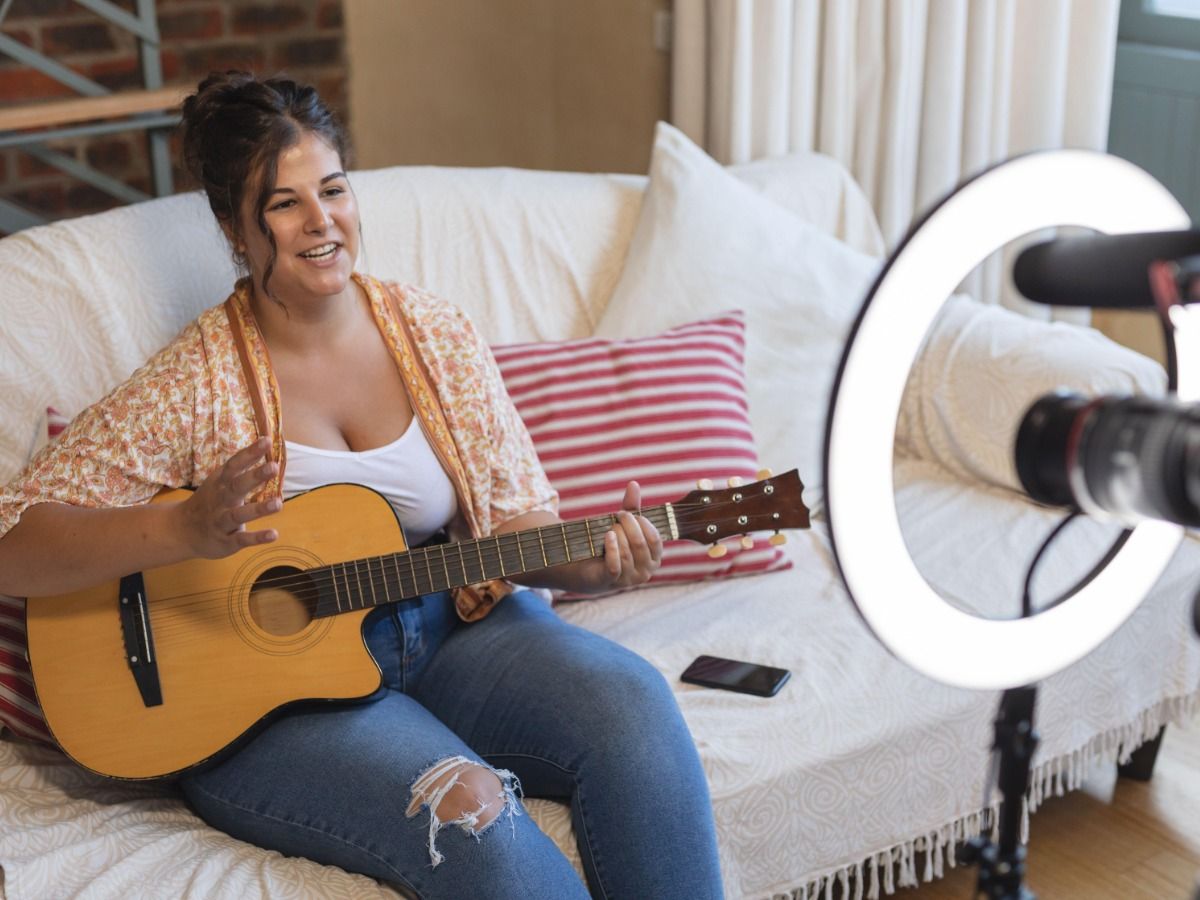 A young woman filming herself playing the guitar - Essential video marketing tips for beginners - Image